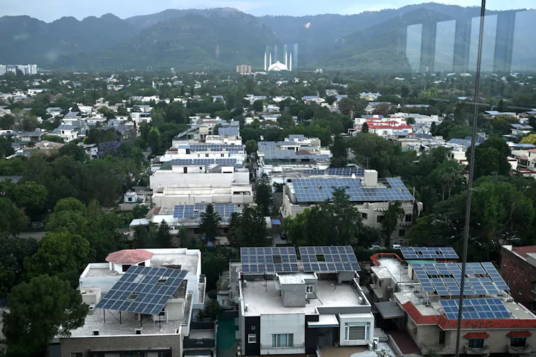 An aerial view of a city shows many buildings with solar panels on their roofs.