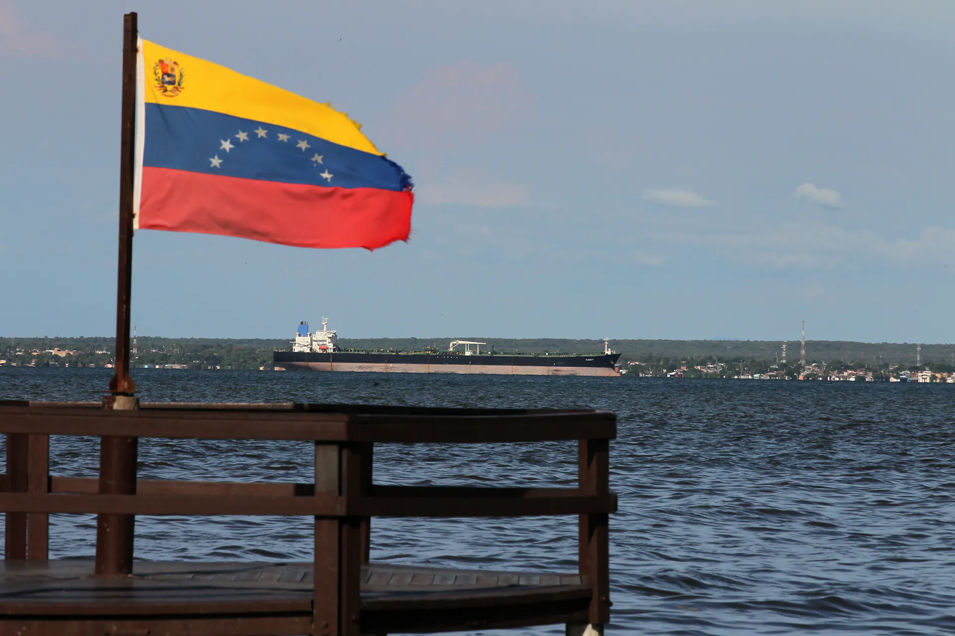 A white, blue and red flag flies in the foreground with a large tanker ship floating in the distance.