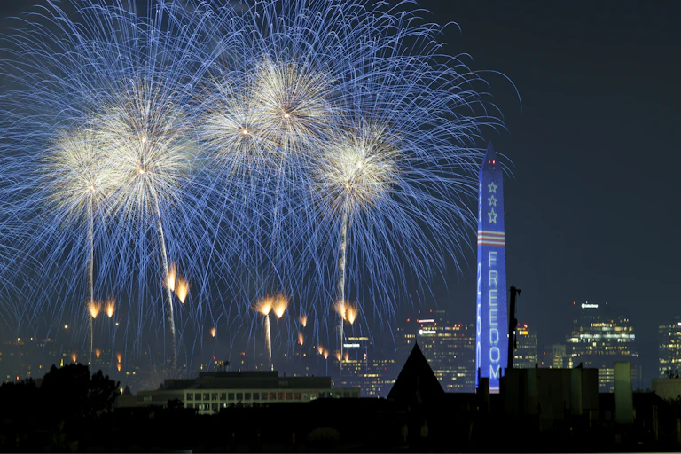 Fireworks go off against a dark sky with the word 'freedom' projected onto a monolith in the foreground.