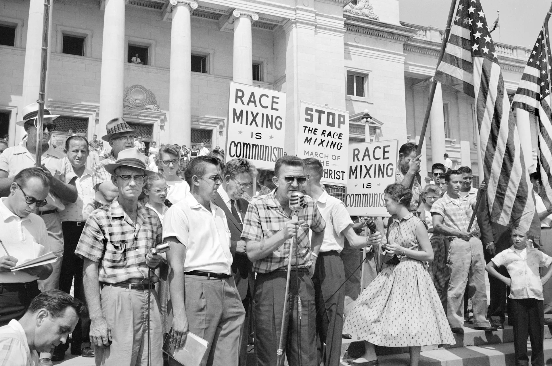 Crowd at Arkansas State Capitol protesting integration, with signs reading 'Race mixing is Communism' and 'Stop the race mixing.'