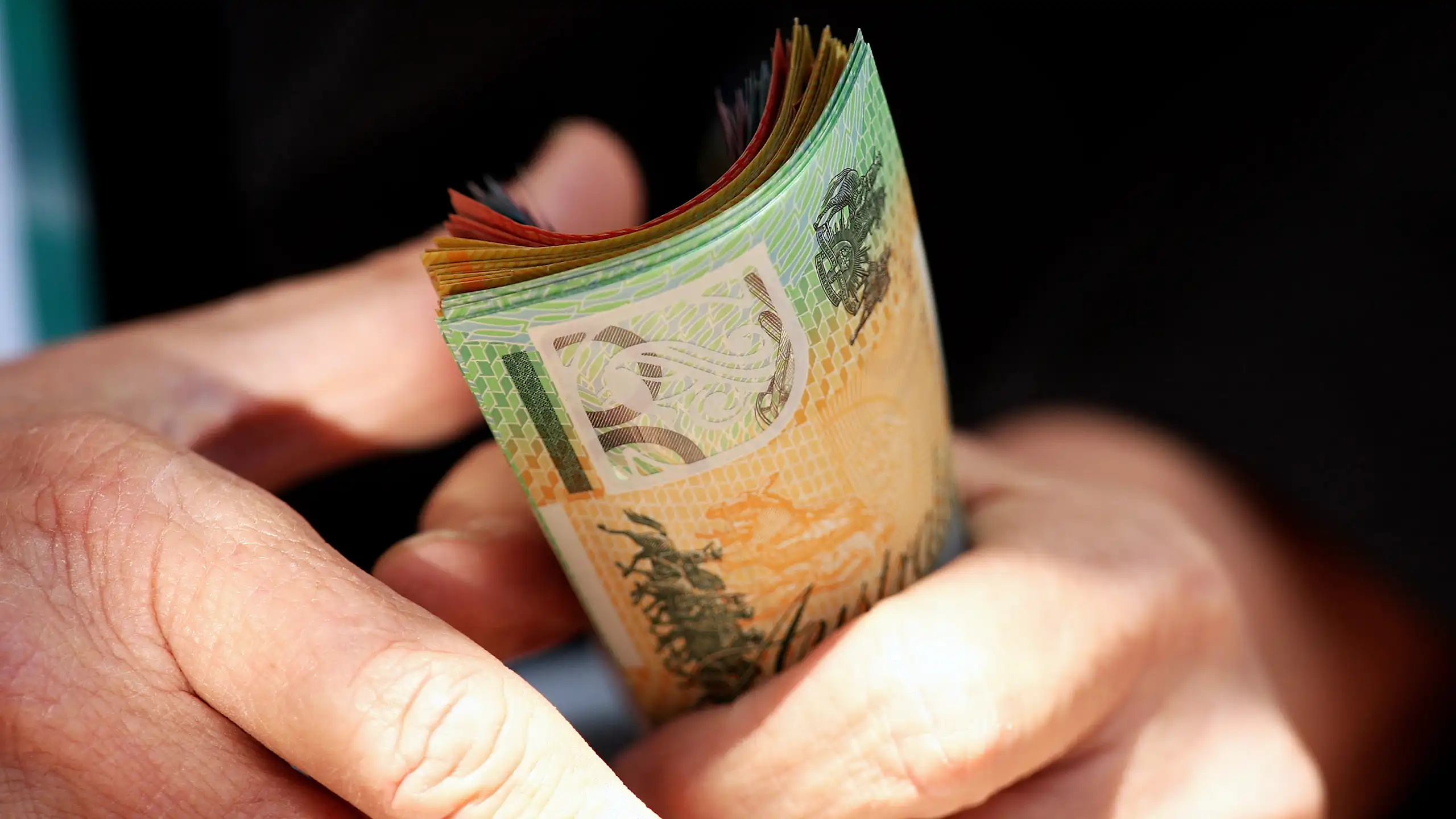 An older person holding a fistful of Australian bank notes worth hundreds of dollars