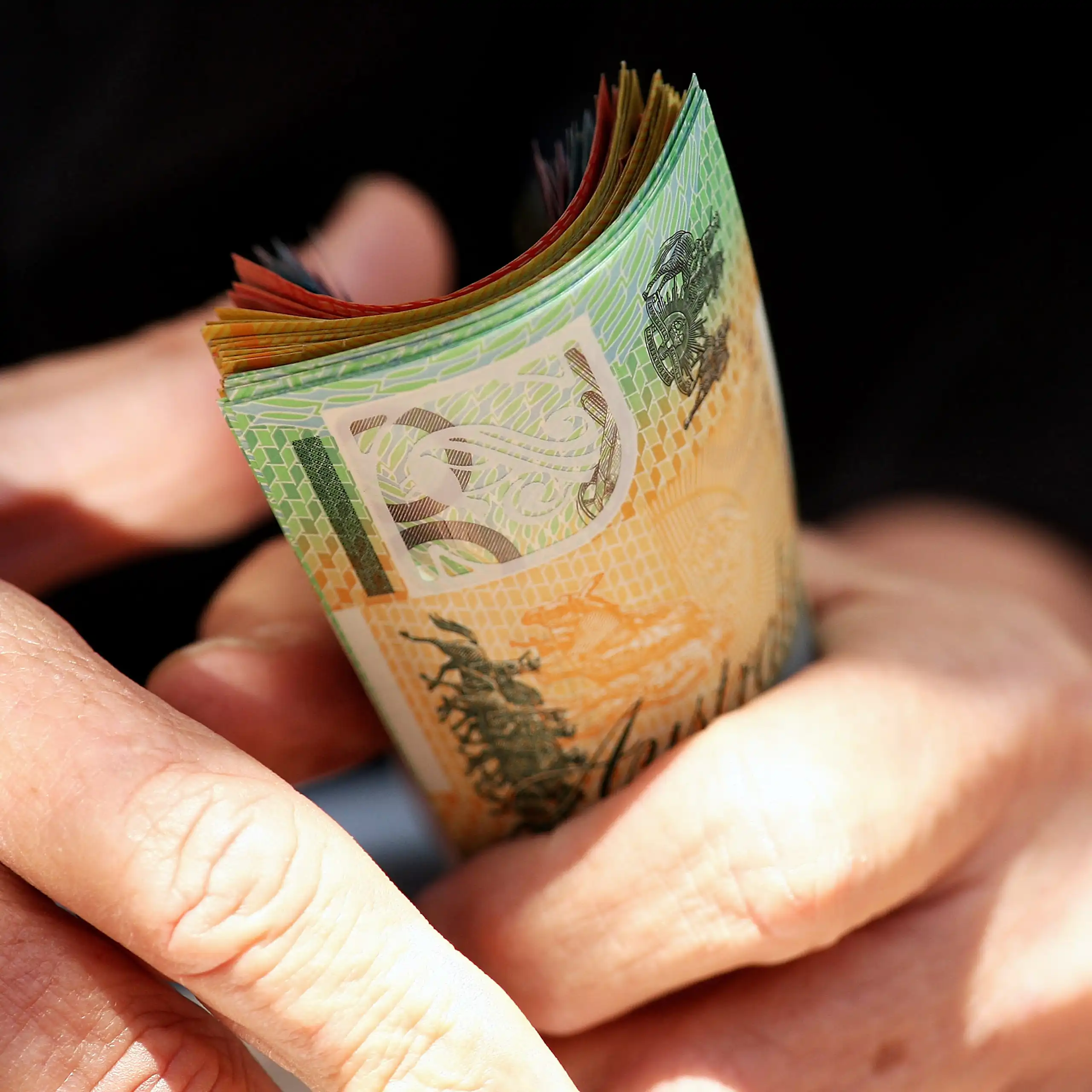 An older person holding a fistful of Australian bank notes worth hundreds of dollars