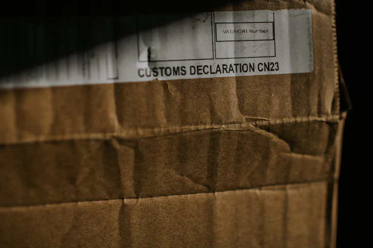 A close up of a dimly lit cardboard box with a customs declaration sticker on it