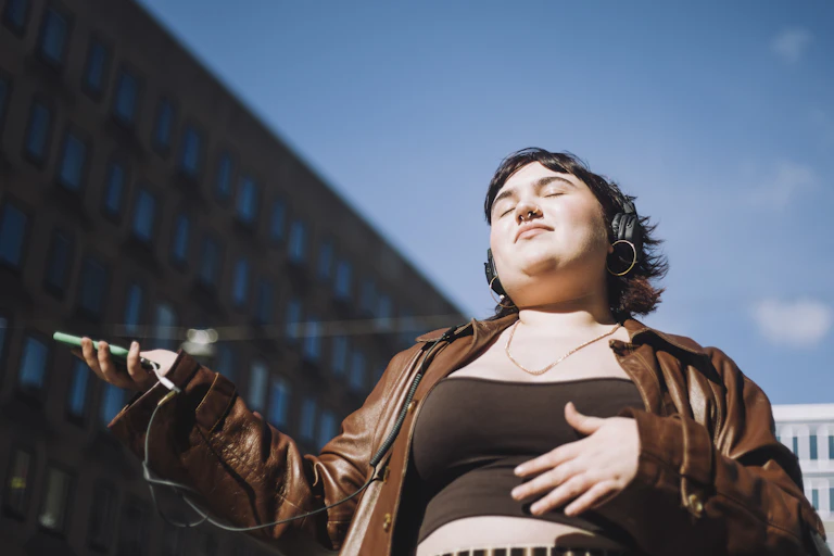 A person basks in the sunlight while listening to music.