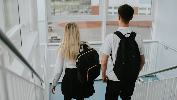 A male student and a female student descend the stairs in a high school building.
