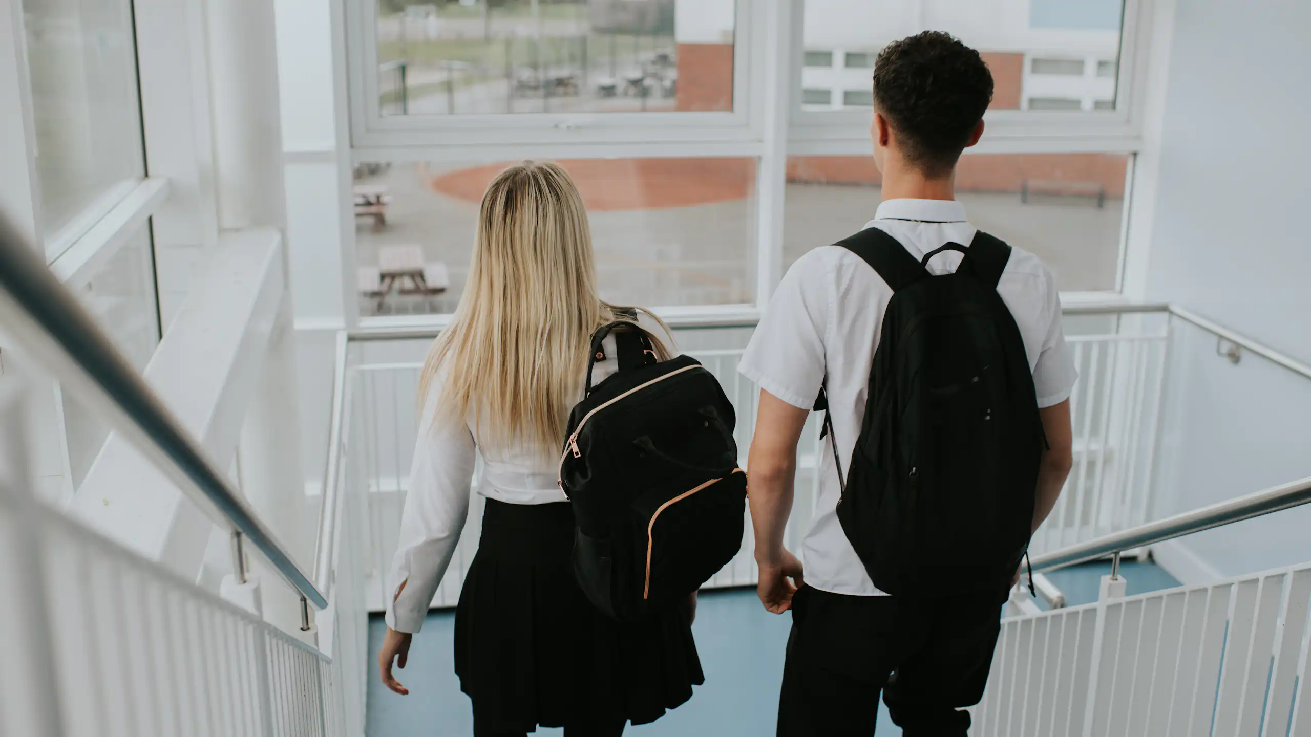 A male student and a female student descend the stairs in a high school building.
