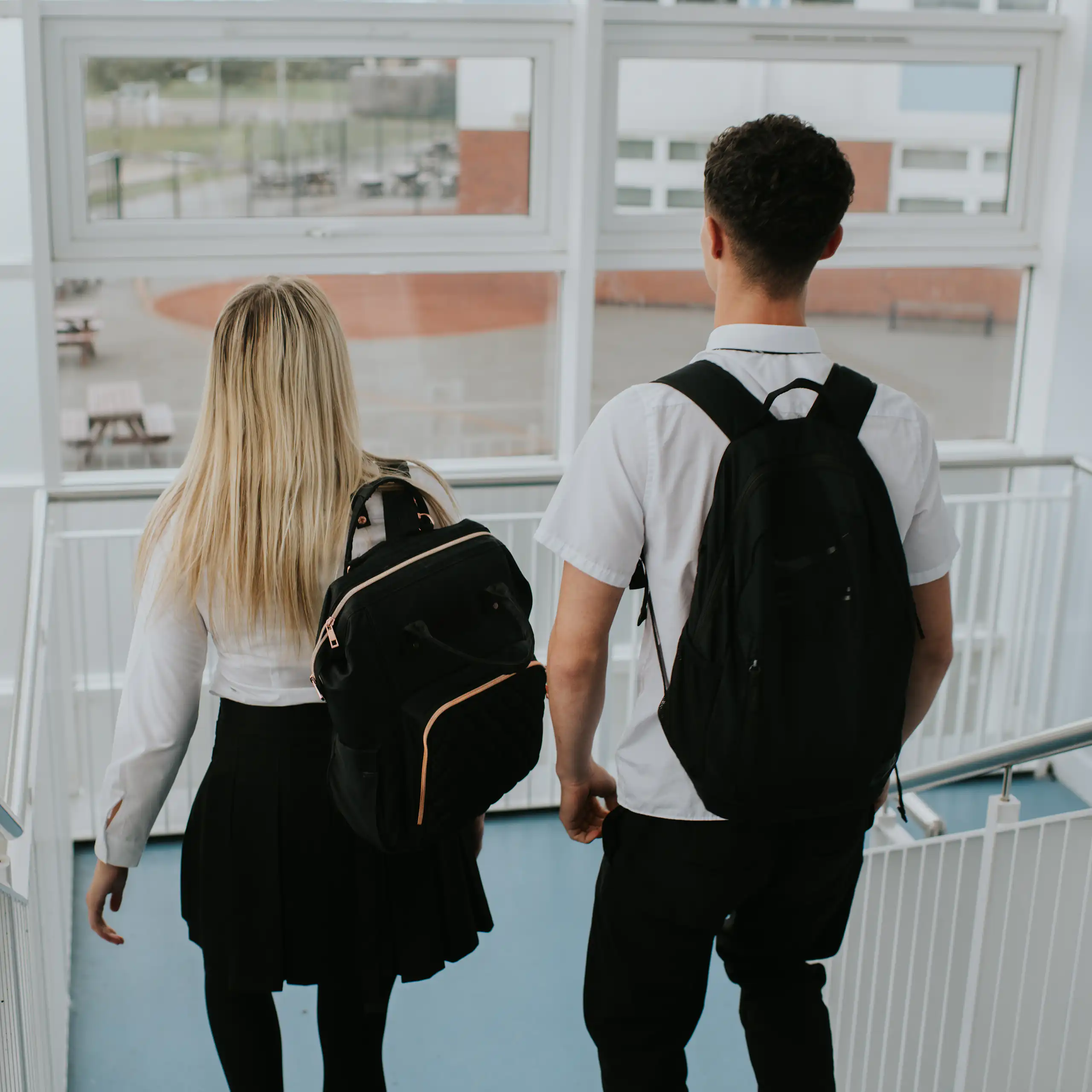 A male student and a female student descend the stairs in a high school building.