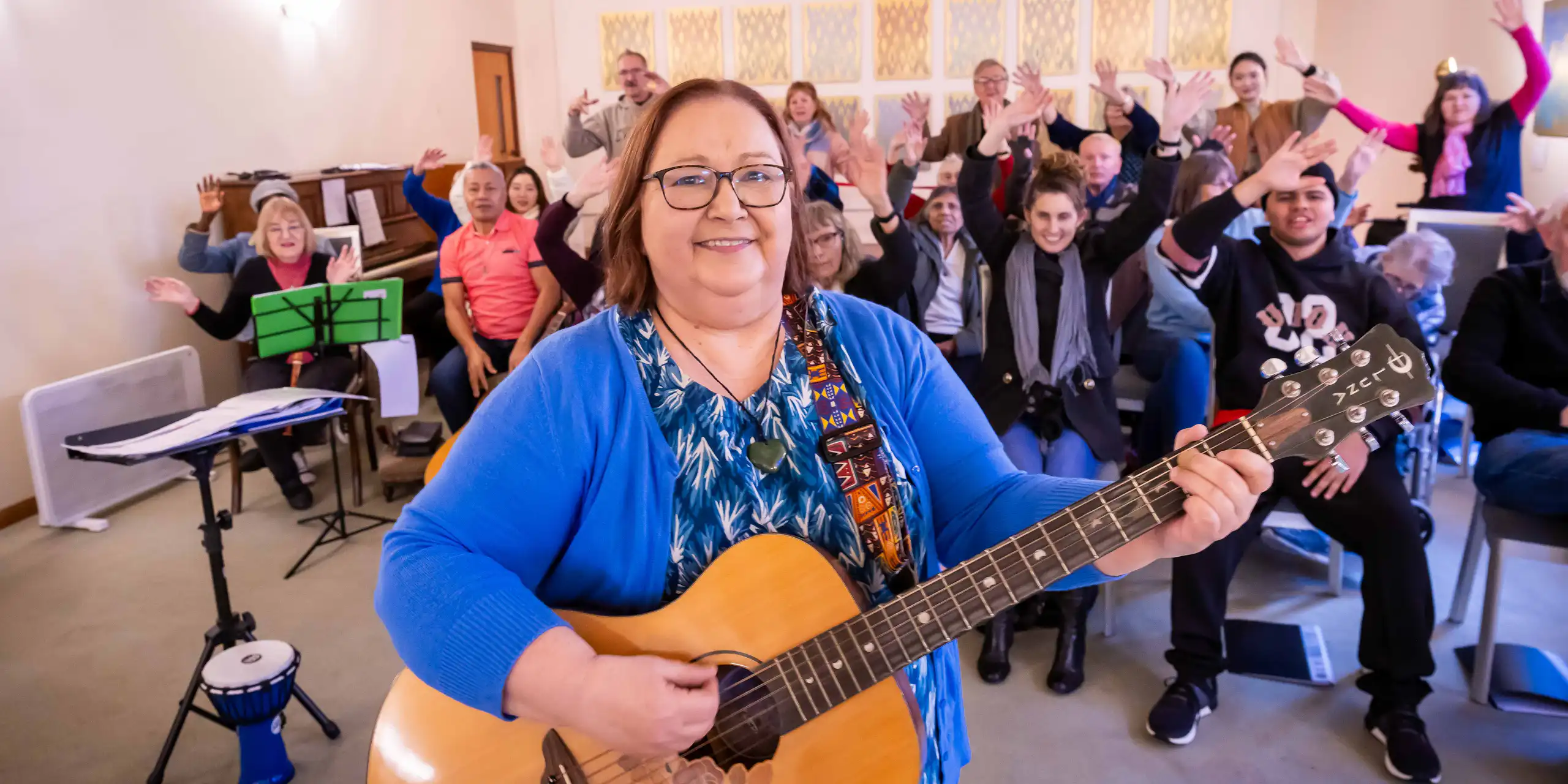 A person playing guitar in the foreground, with a seated choir in the background