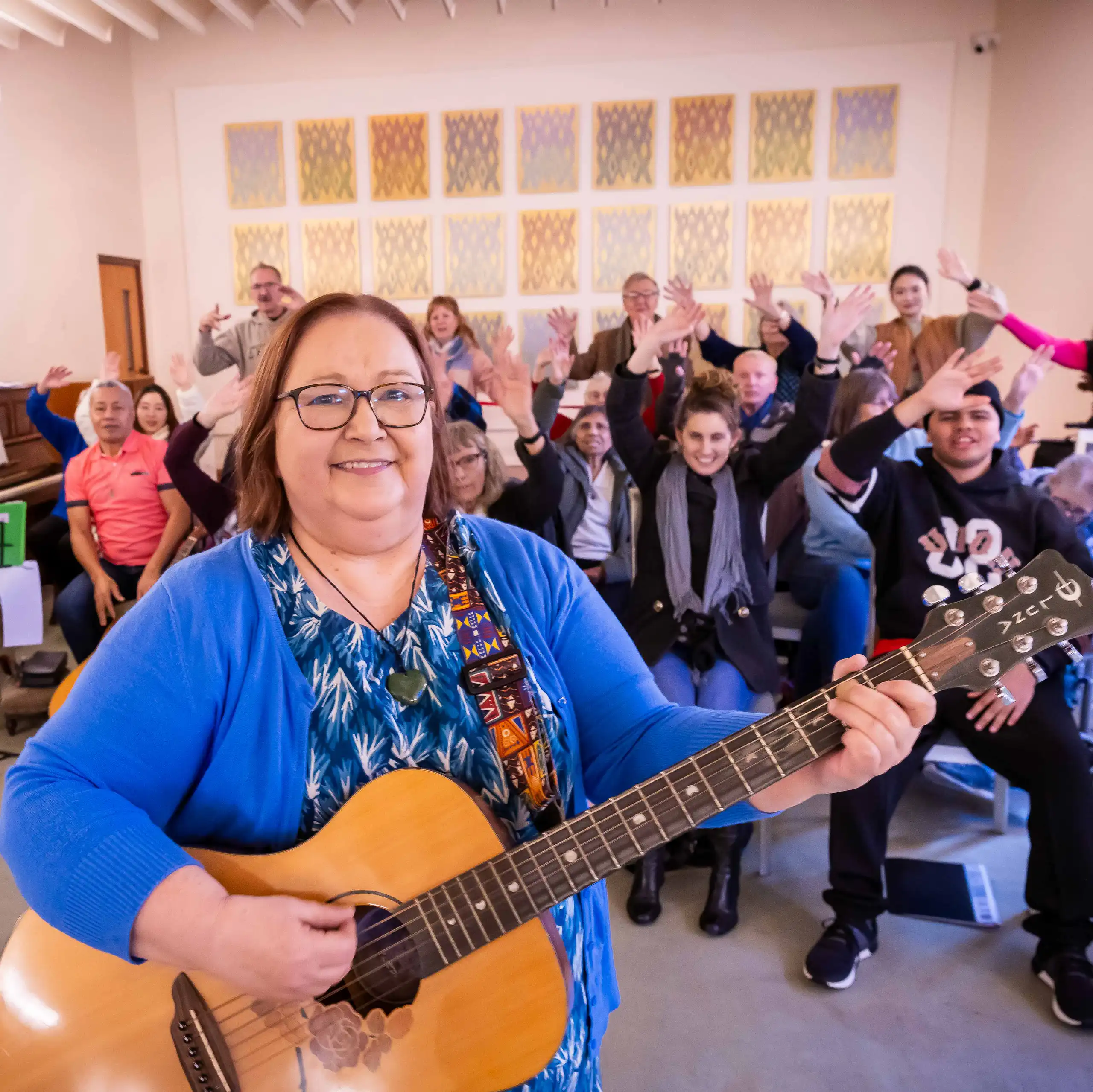 A person playing guitar in the foreground, with a seated choir in the background