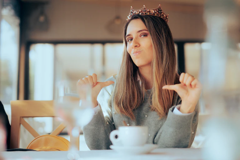 A confident-looking woman drinking tea while wearing a crown.