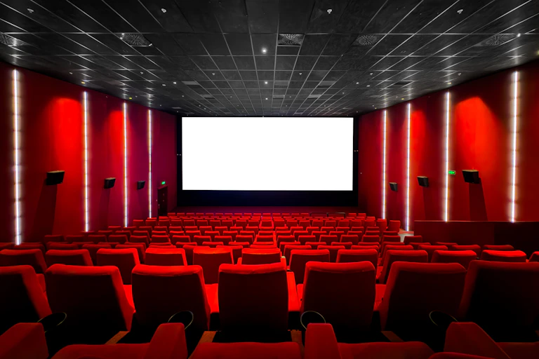 The interior of a cinema with red velvet seats and a blank white screen.