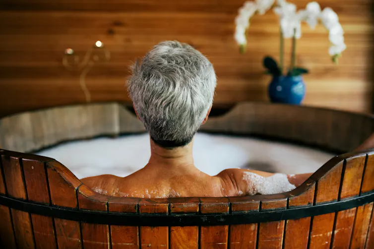 A grey haired person shown from behind sitting in a warm bath.