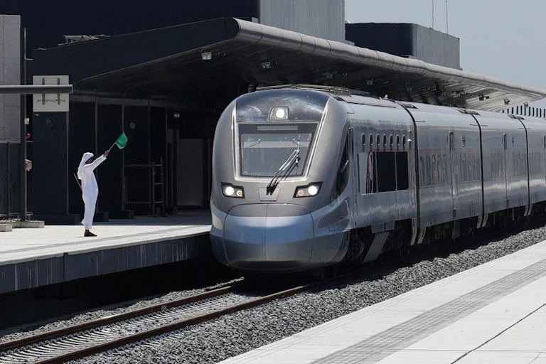 A man in traditional Emirati dress waves a flag at a train.