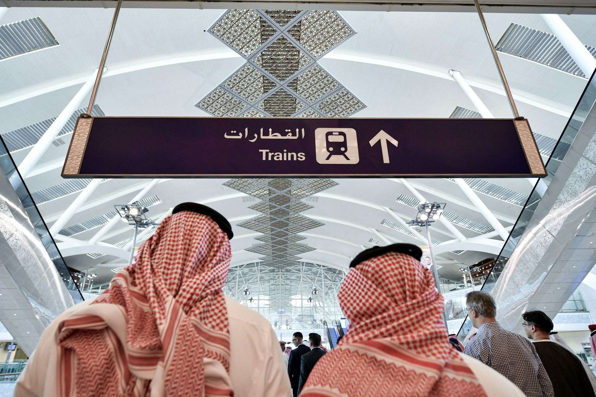 Two men in traditional Arab dress look at a train sign.