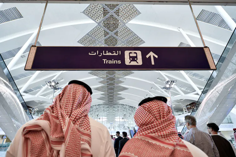 Two men in traditional Arab dress look at a train sign.