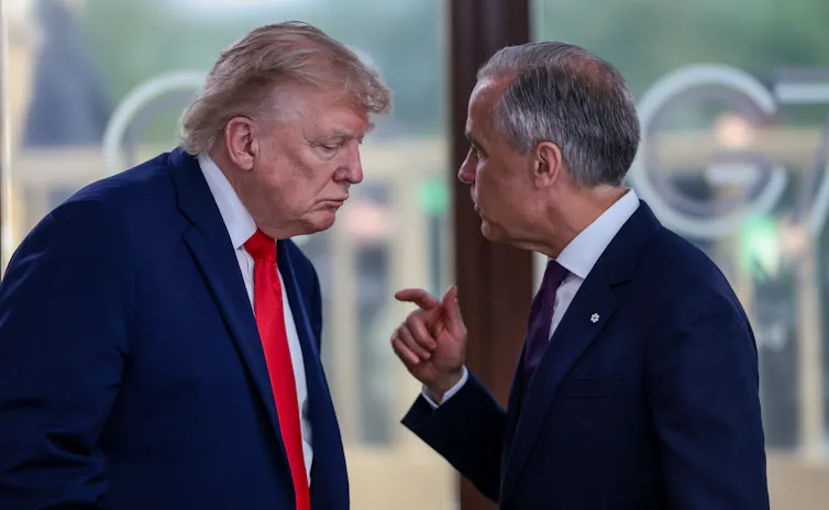 A slender man with short grey hair holds his finger up while talking to a hulking older man with yellow-ish white hair.
