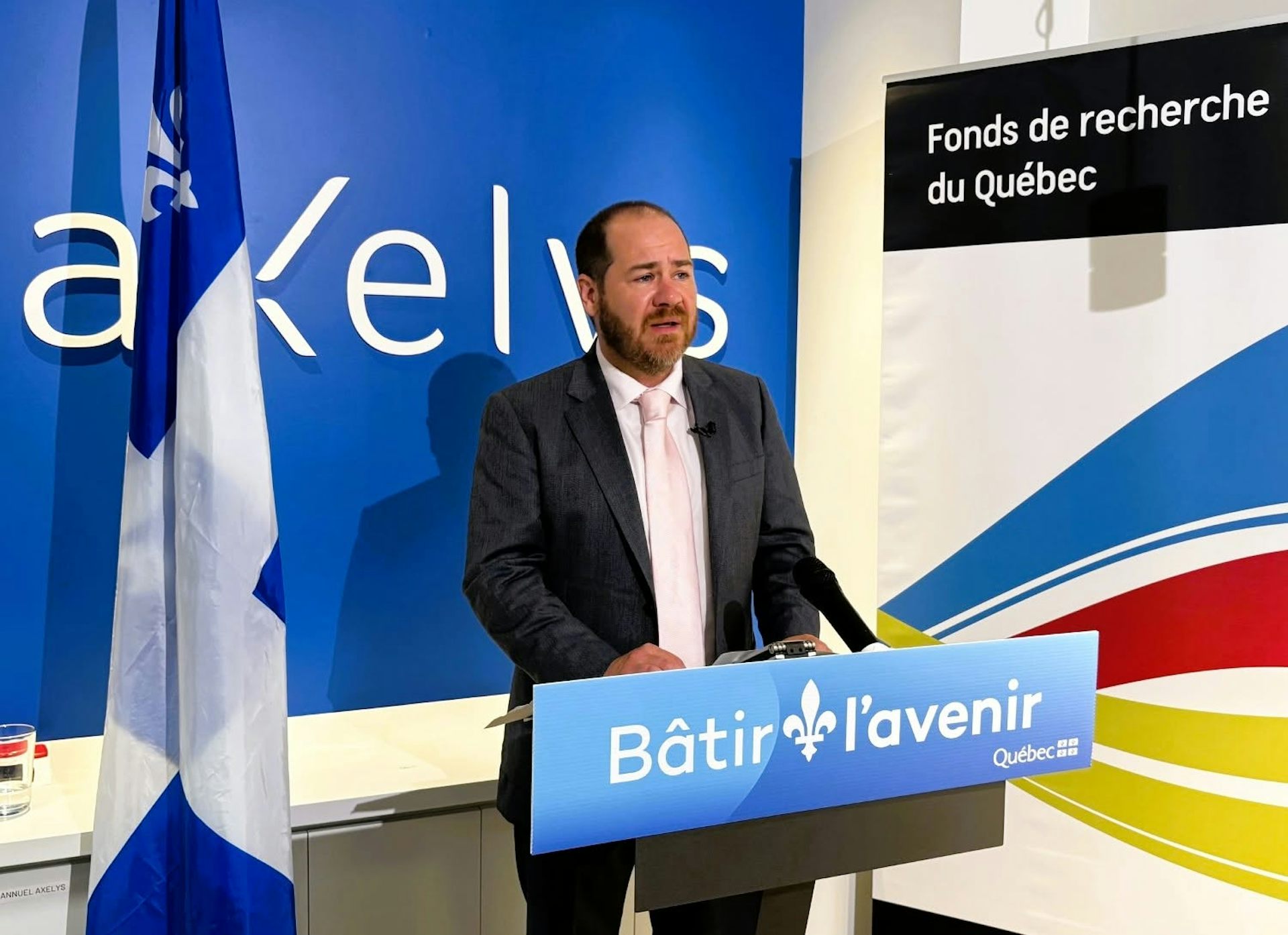 Jérôme Dupras est debout devant un micro, avec des affiches à l’arrière-plan