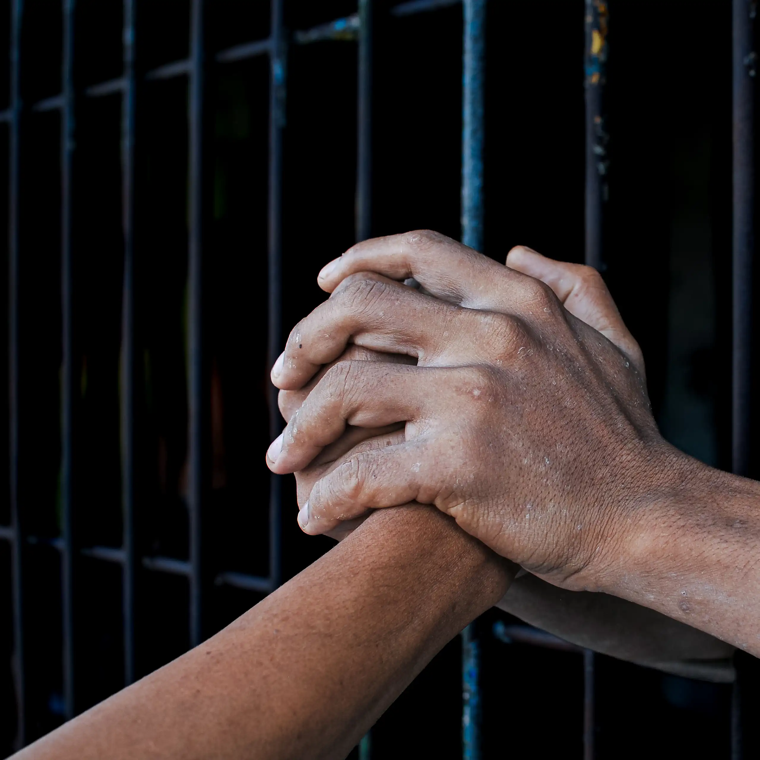 Two hands clasp another hand, with bars separating the two individuals.