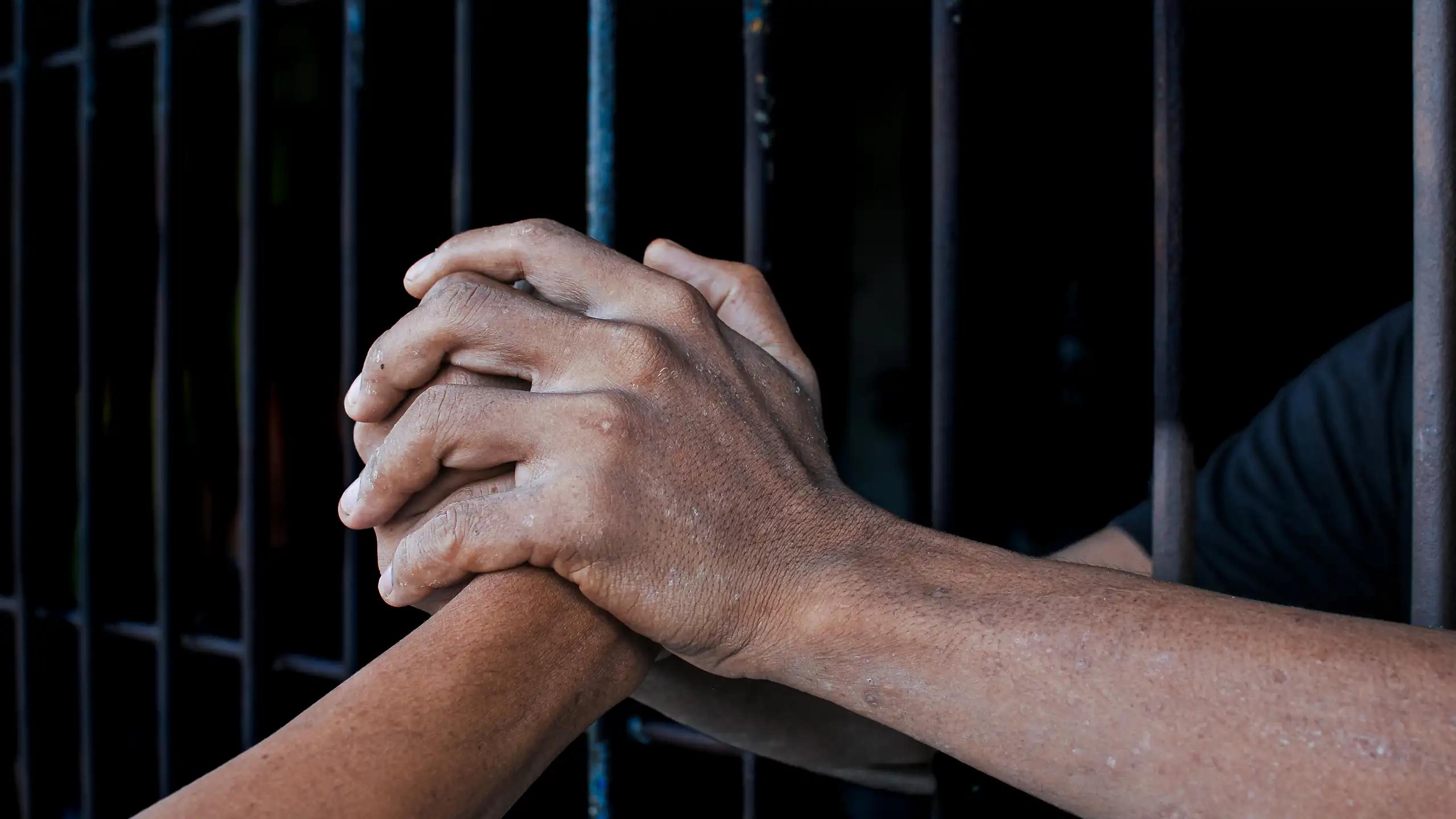 Two hands clasp another hand, with bars separating the two individuals.