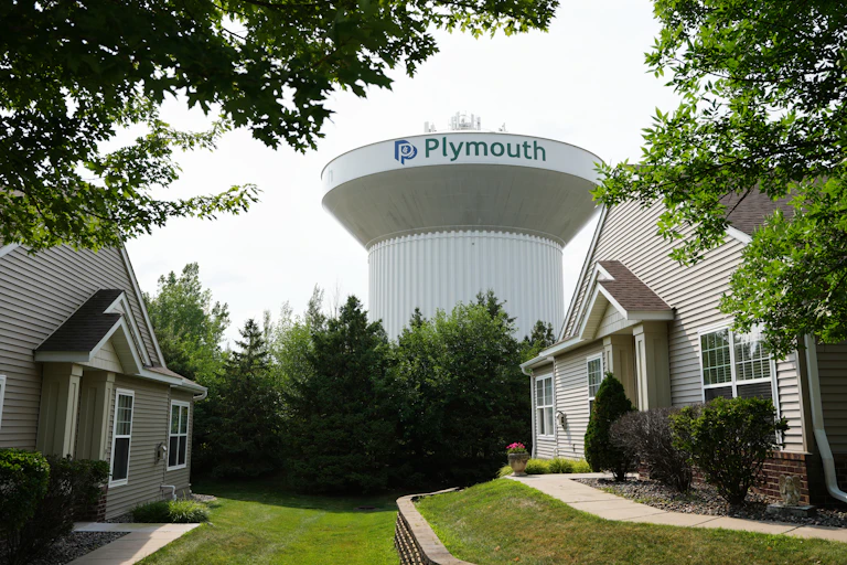 a large cylindrical structure behind a row of trees with two houses in the foreground