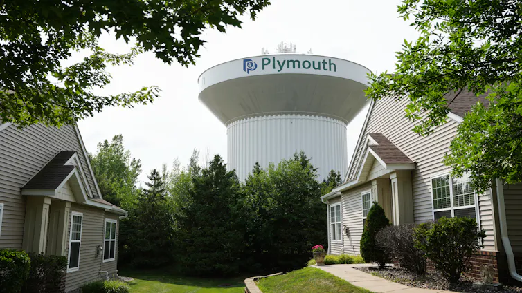 a large cylindrical structure behind a row of trees with two houses in the foreground