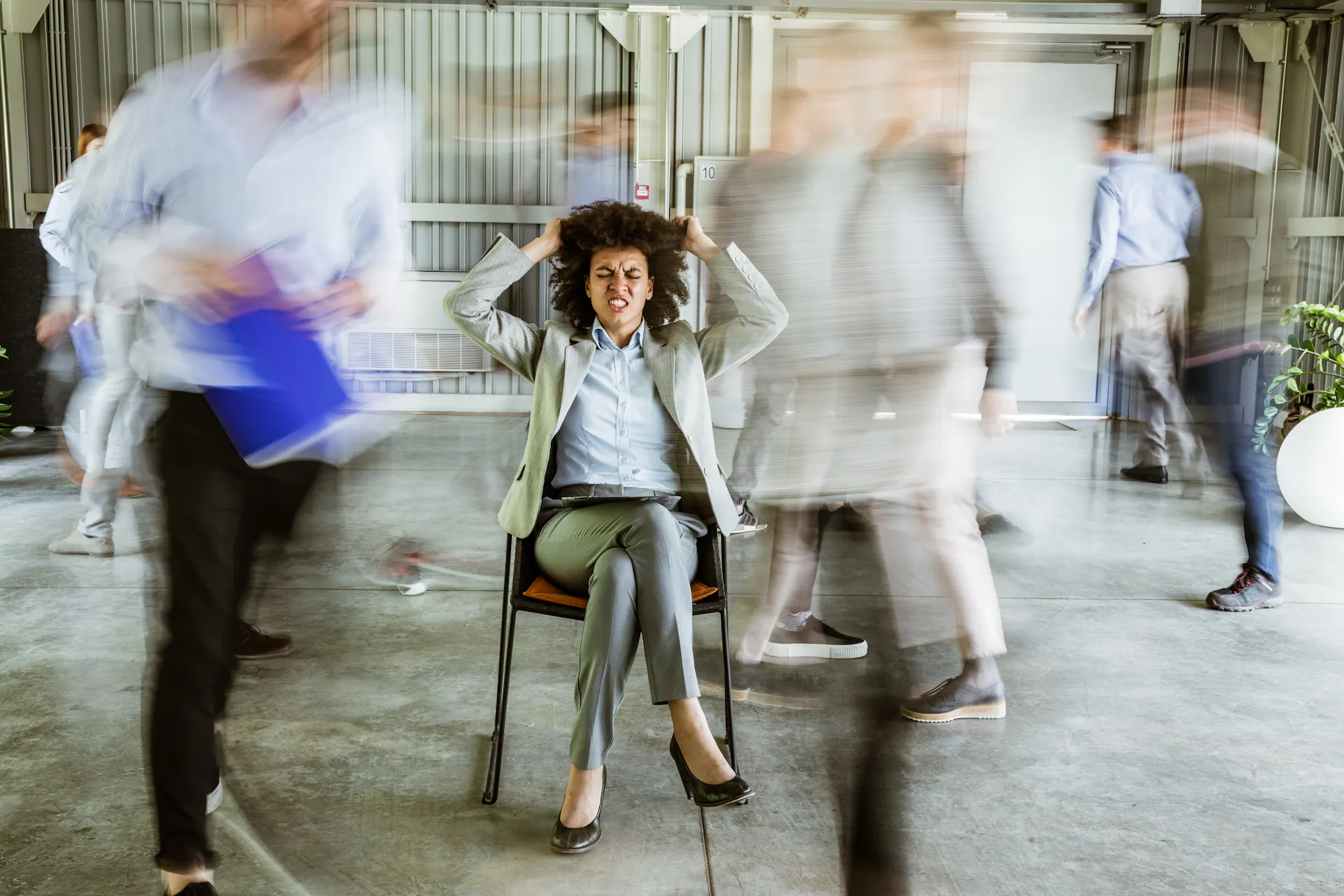 A woman clutches her head in frustration as blurred colleagues walk by