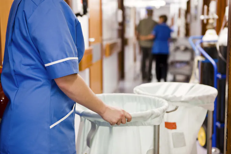 A woman rolls laundry bins down a hospital hallway.