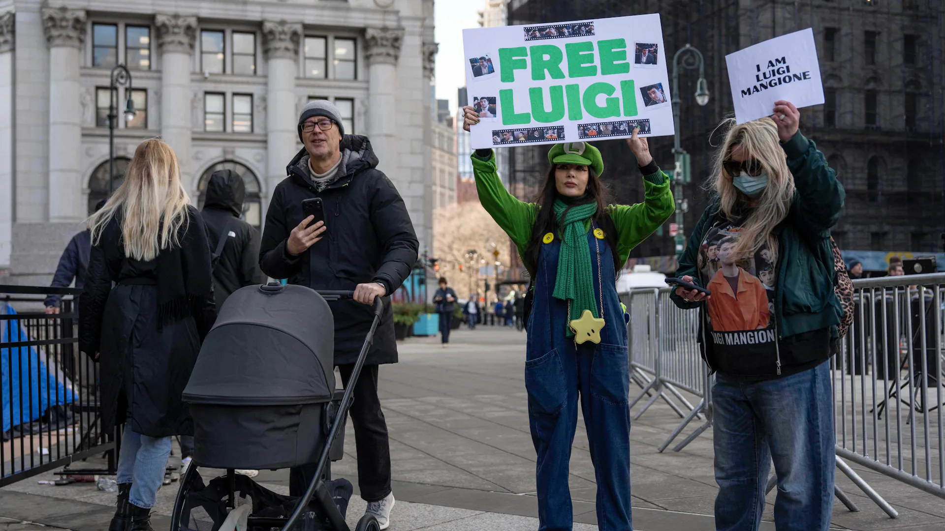 One person dressed in a green Luigi costume holds a 'FREE LUIGI' sign, while another holds a sign reading 'I AM LUIGI MANGIONE.'