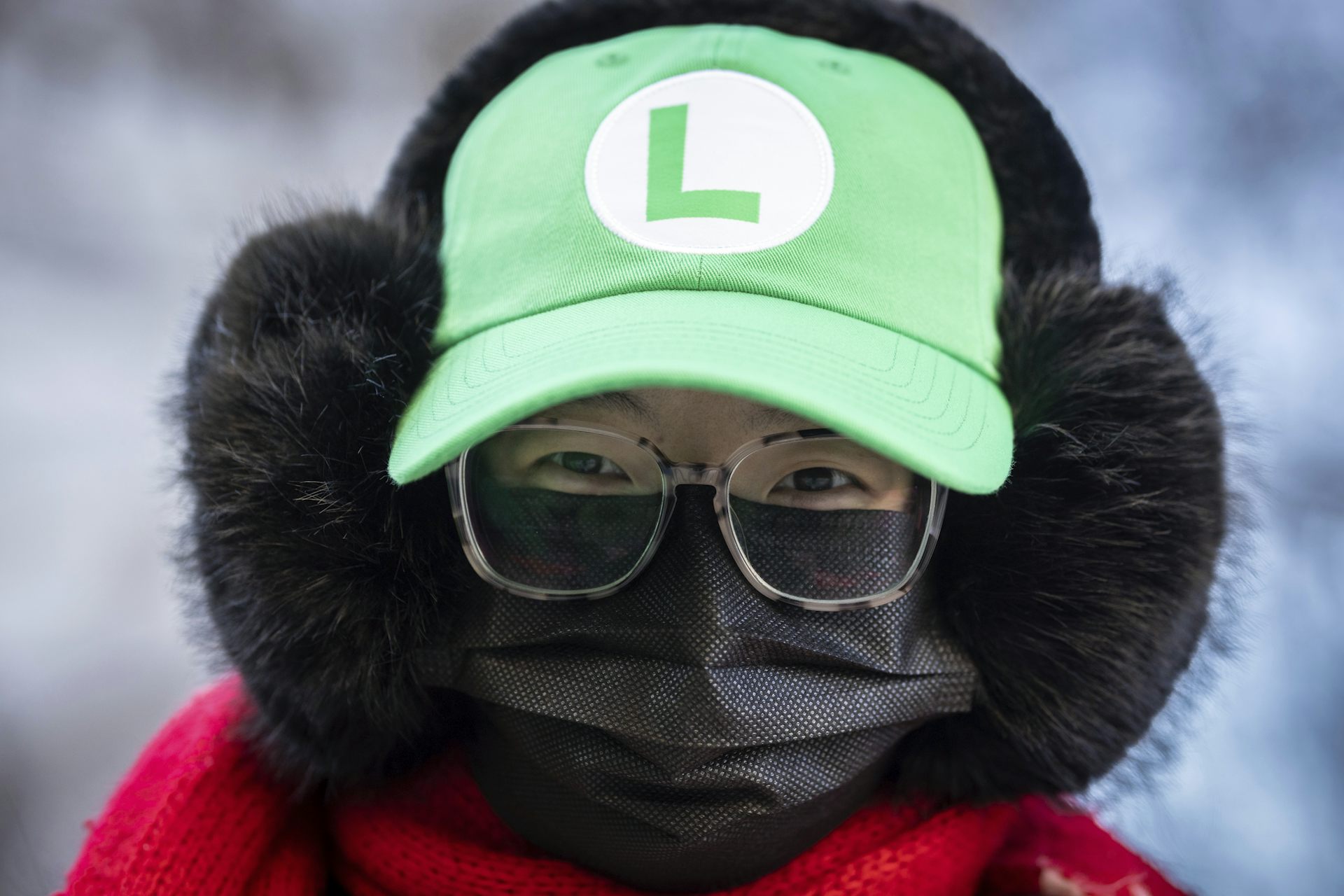 A supporter outside court wears eyeglasses, a black face mask and a green hat with an 'L' logo