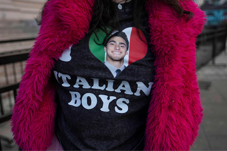 A person wearing a black t-shirt that features a heart graphic with an Italian flag and a portrait of Luigi Mangione