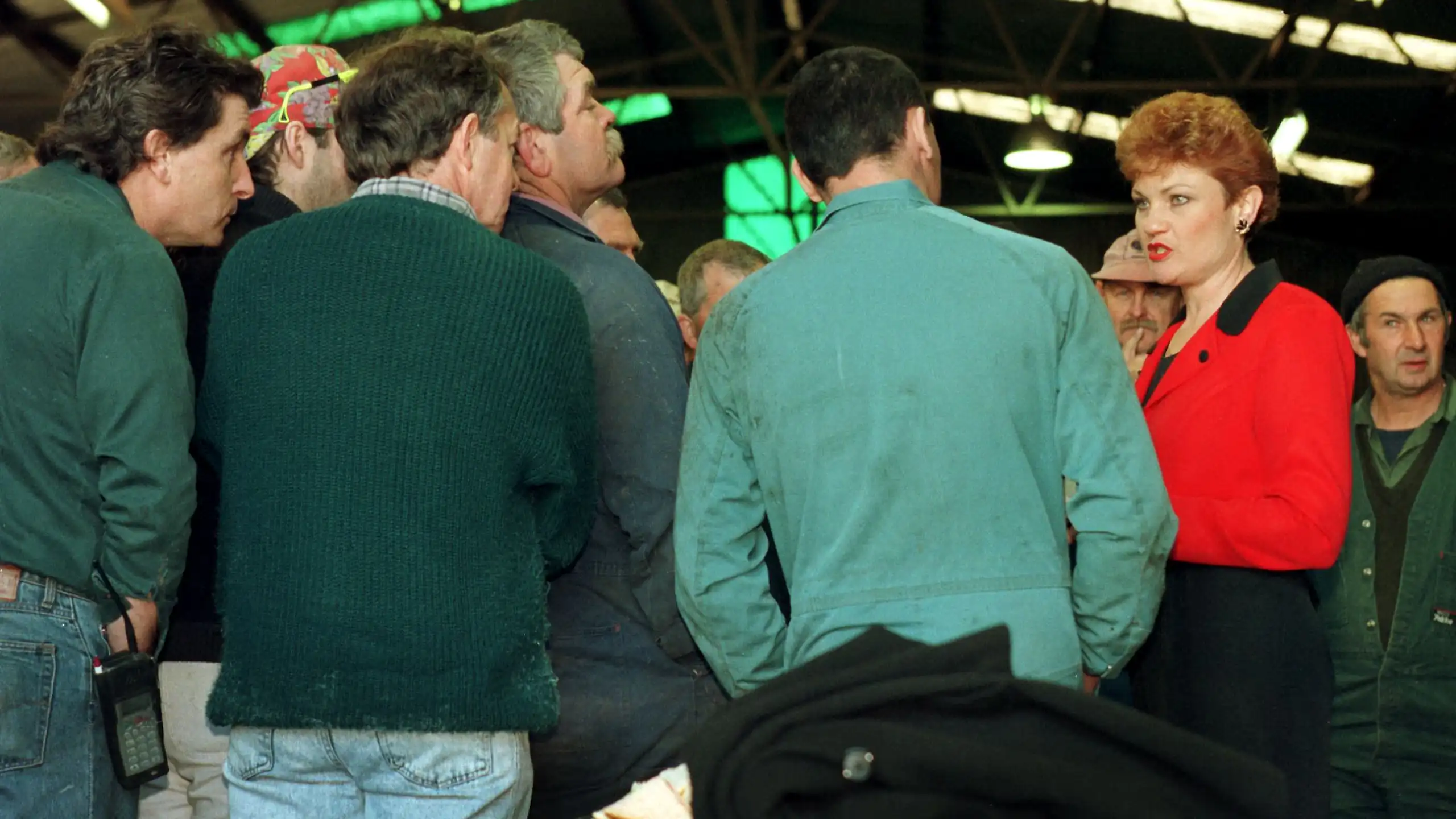Pauline Hanson, in a bright red top, speaks to a crowd of white men