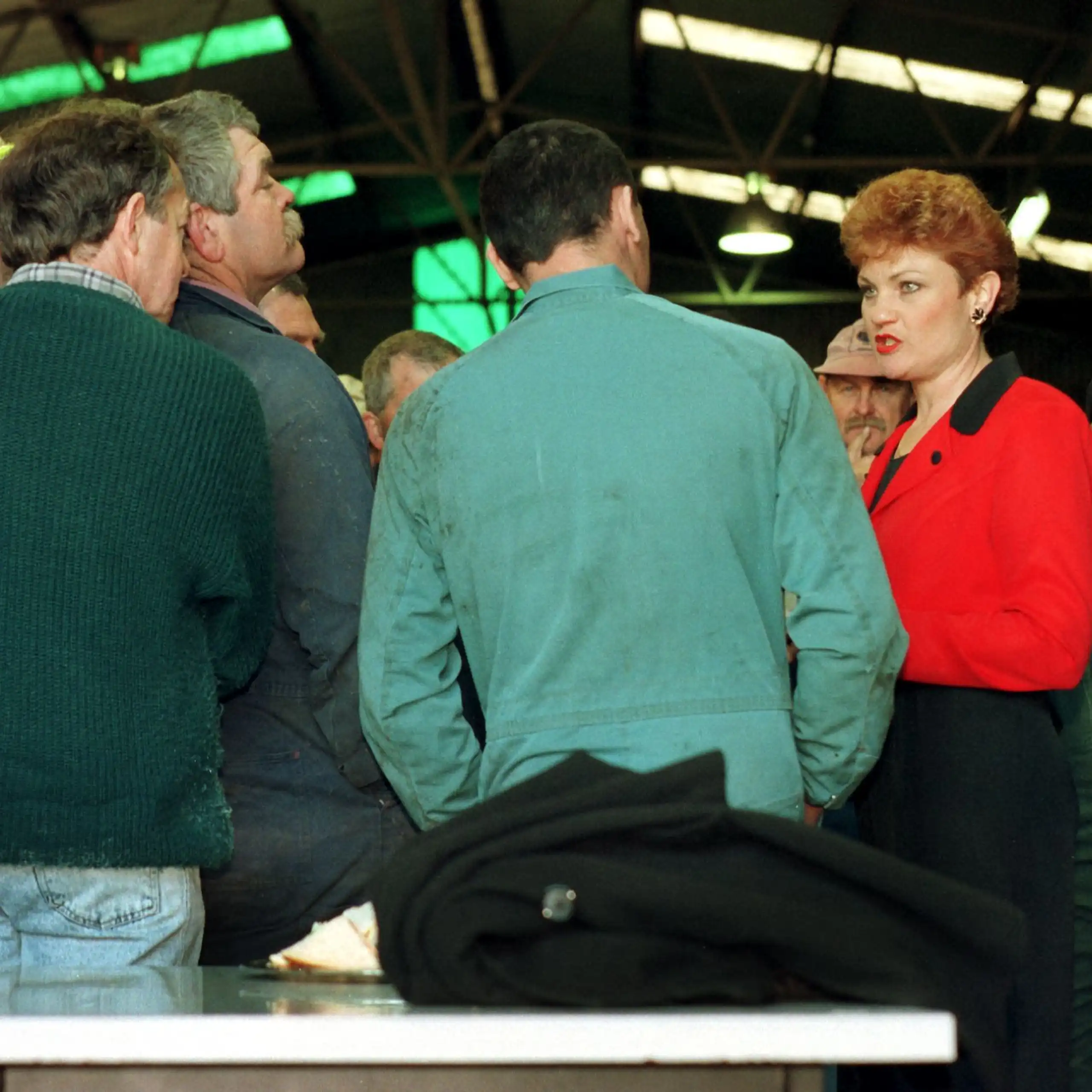 Pauline Hanson, in a bright red top, speaks to a crowd of white men