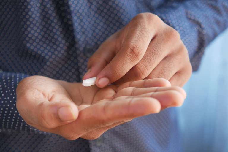A man holds a white pill in his fingers. He's about to place it in his palm.