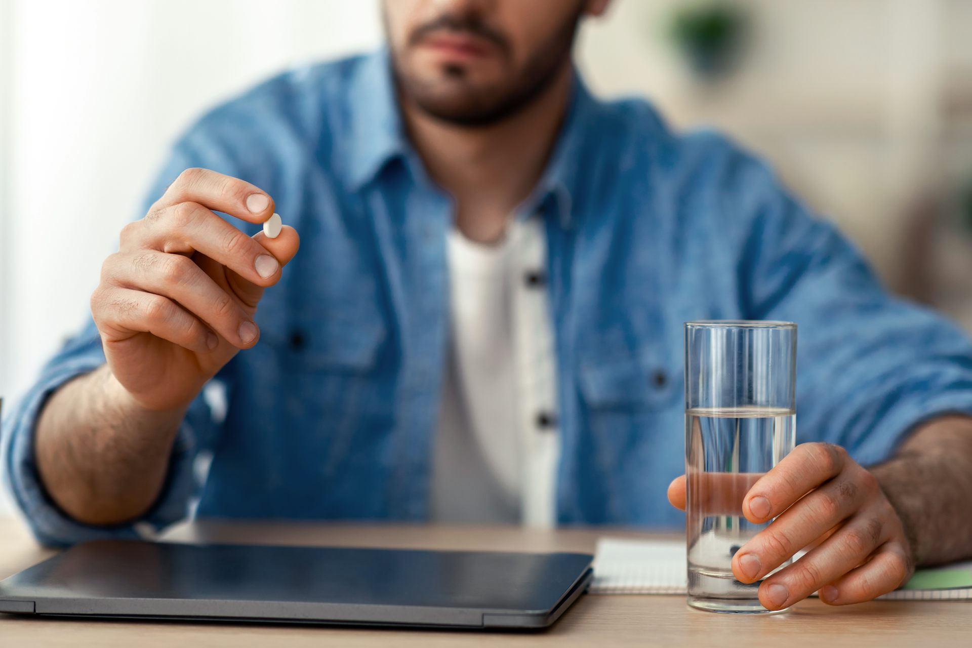A man holds up a pill in his one hand. In the other hand, he's holding a glass of water.