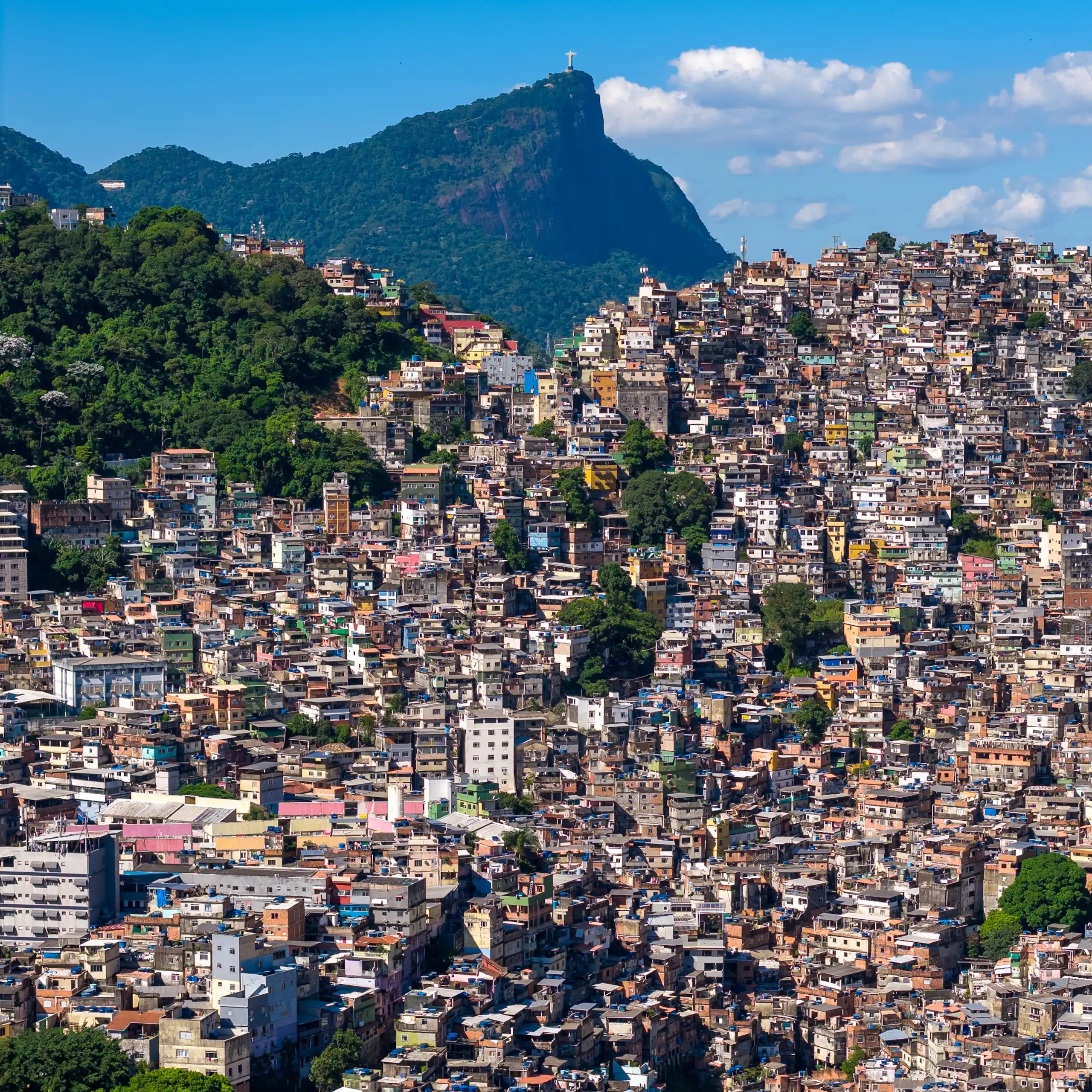 A favela on a steep hillside of Rio against a blue sky and mountains.