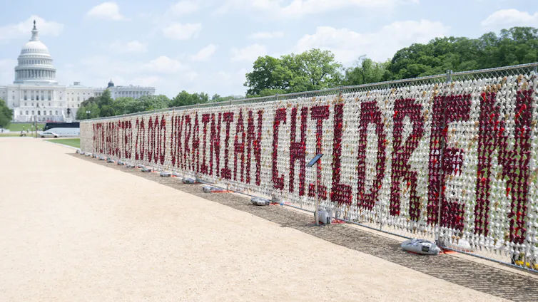A fence featuring 20000 stuffed teddy bears that spell out 'Putin abducted 20,000 Ukrainian children.'
