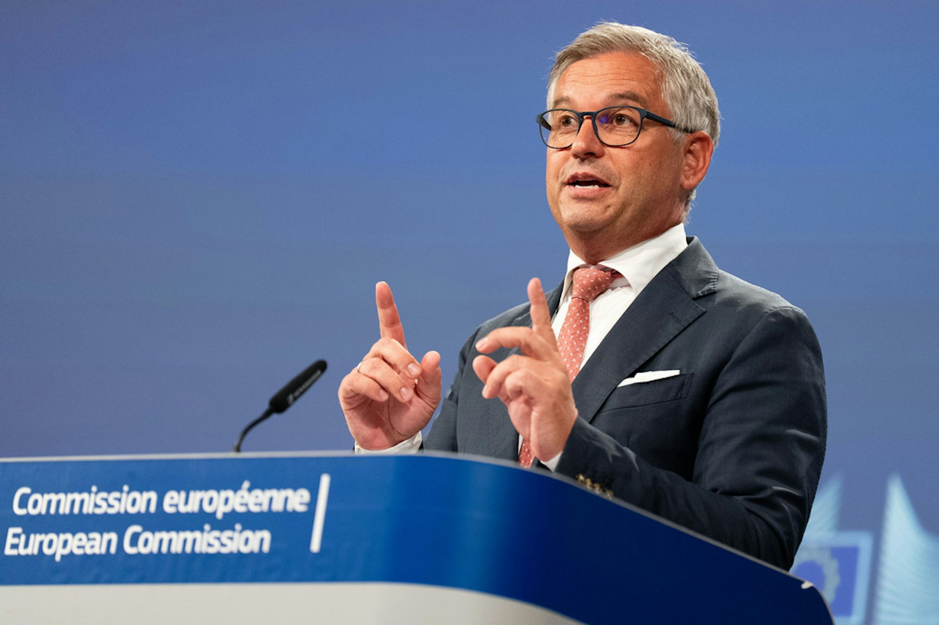 A man in a suit stands at a lectern.