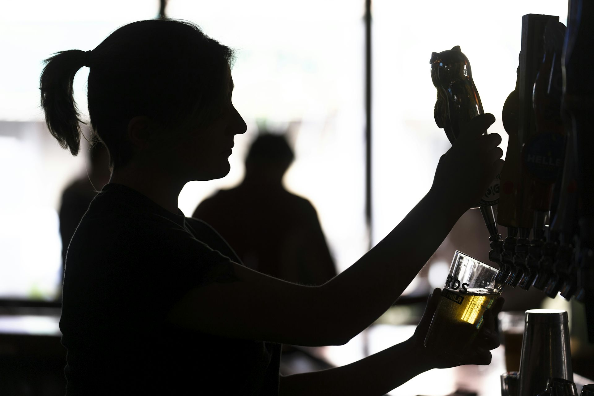 Silhouette of a bartender filling a glass with beer from a tap