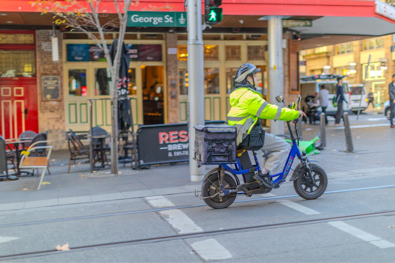 A food delivery rider, on a bicycle, rides along a street in Sydney