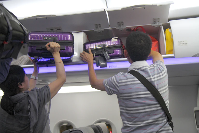 Asian man and woman removing luggage from carry-on overhead luggage bin.