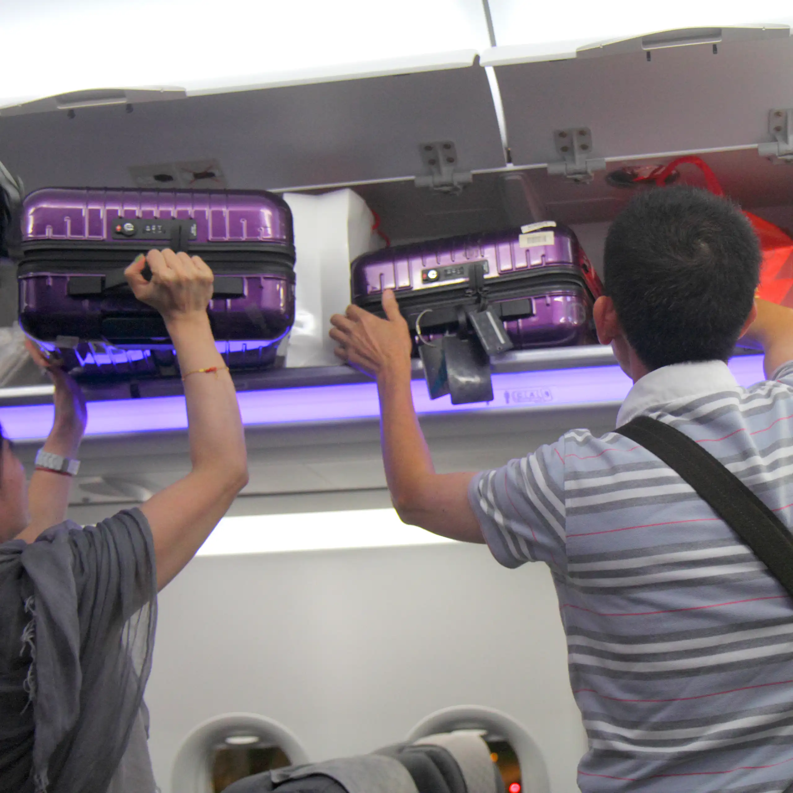 Asian man and woman removing luggage from carry-on overhead luggage bin.