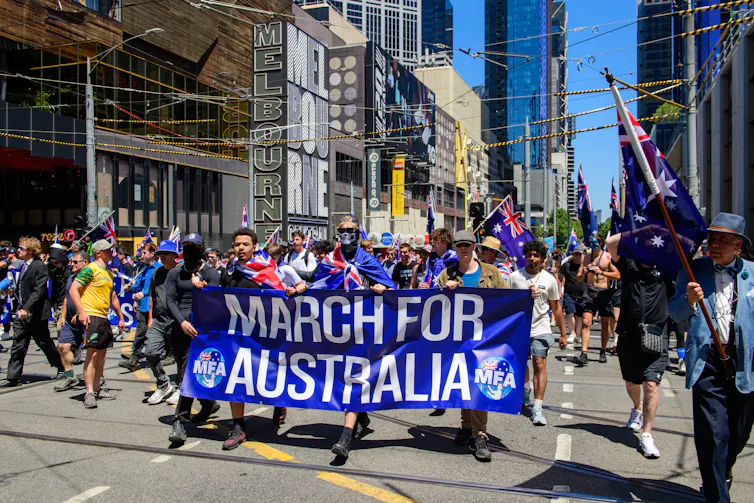 A group of protesters in a city street, waving Australian flags and holding a large banner that says March for Australia