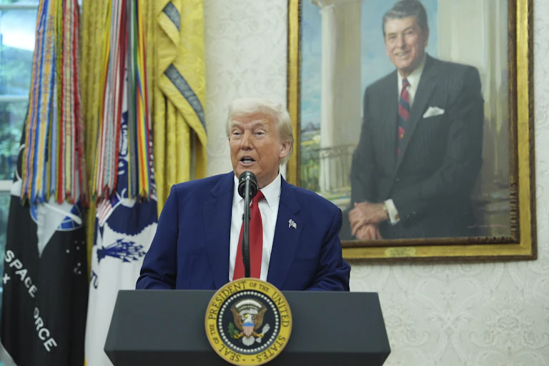 Donald Trump speaks at a lectern bearing the presidential seal with a painting of Ronald Reagan in the background