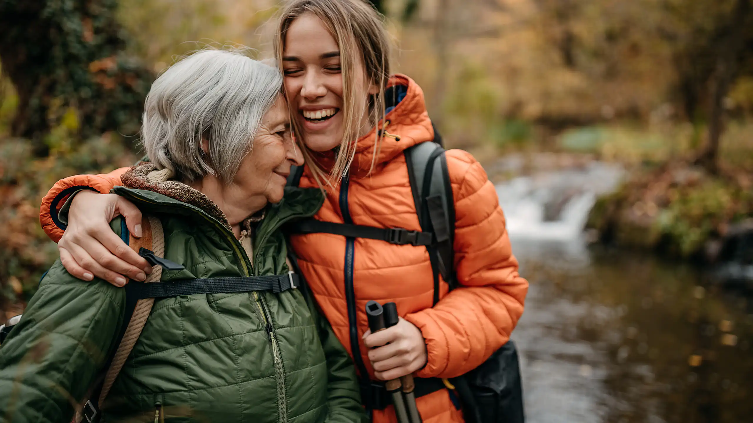 Older woman and younger woman hugging, on a hike
