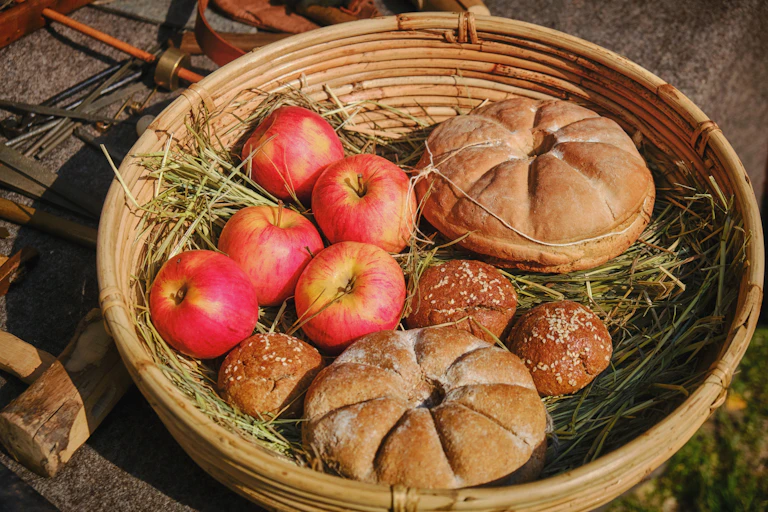Reconstruction of Ancient Roman basket with round bread and red apples on bed of grass