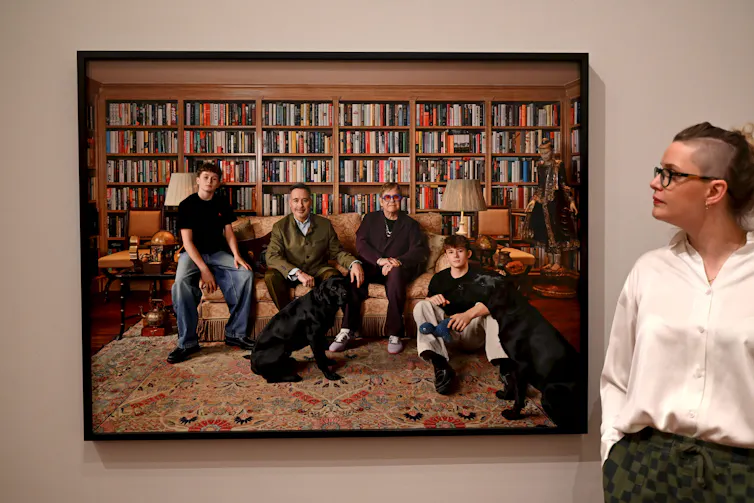 Two adult men and their teenage sons sitting on a sofa in a library.