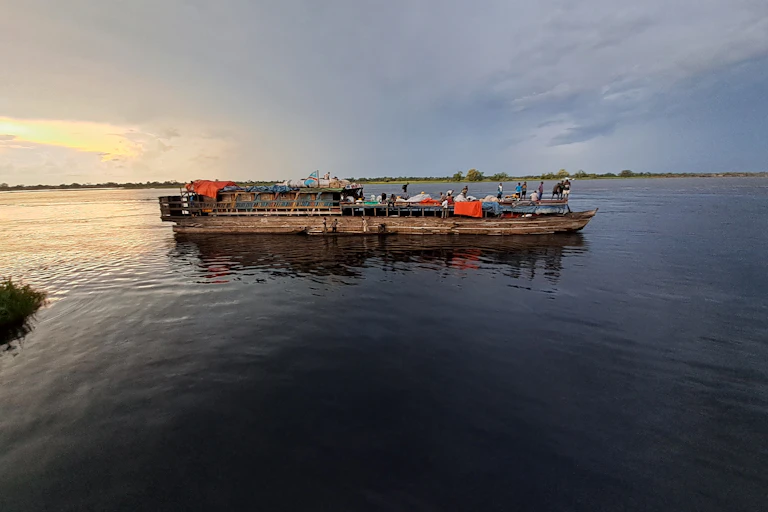 A laden wooden boat floats in an expansive of water.