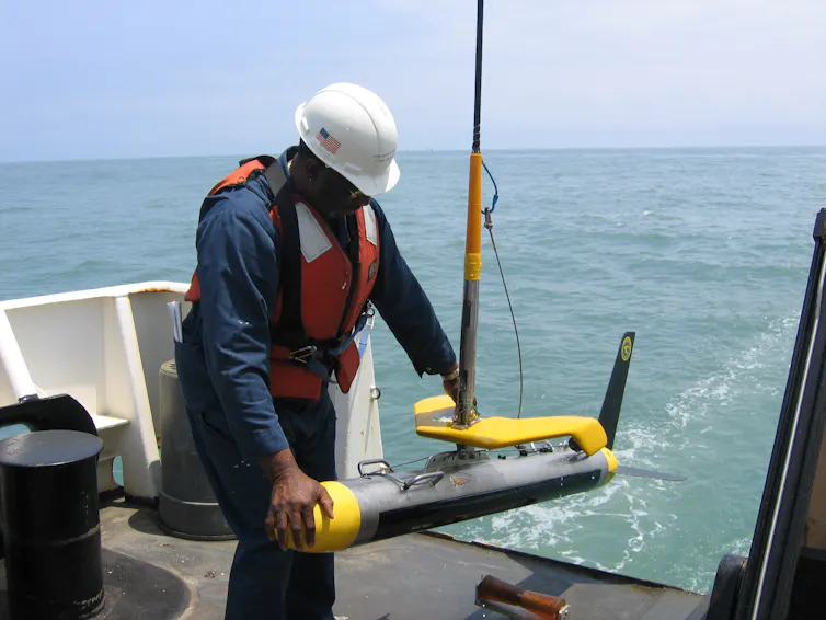 man in hardhat on the back of a boat with scientific equipment in his hands