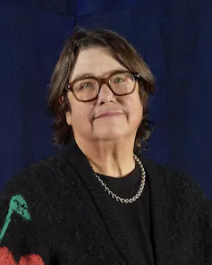 A middle-aged woman in a black jumper smiling faintly at the camera.