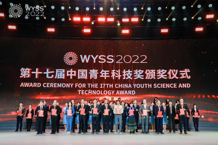 dozens of young people pose on a stage holding awards